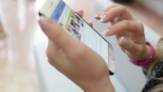 Girl looks through Facebook page on a Mobile Phone - close-up of Hand and Phone