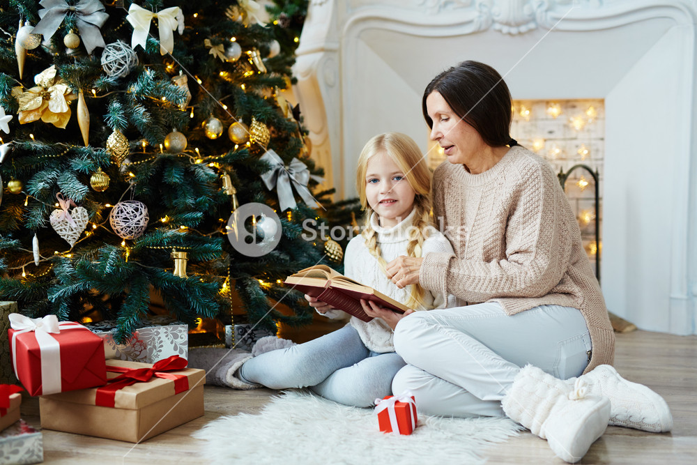 Granny and child reading holiday stories by decorated tree