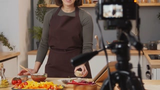 Selective focus shot of female culinary blogger showing food ingredients while filming video recipe in kitchen